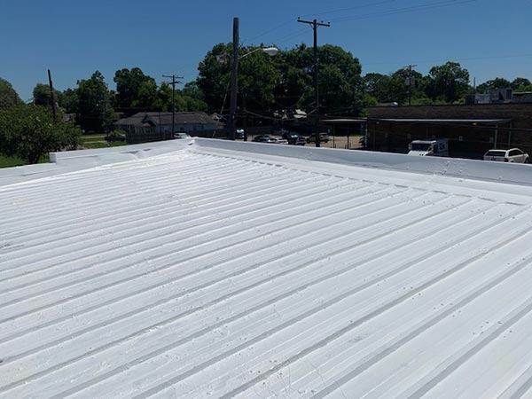 White metal corrugated roof viewed from above with a street and trees in the background.