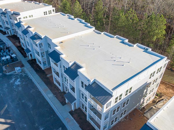 TPO-Roofing-Onalaska-WI-Wisconsin-1 | Golden Eagle Roofing Aerial view of a white and gray apartment building complex with blue roof accents, multiple balconies, and a tree-lined backdrop.